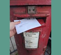 A ballot paper is posted into a red post box